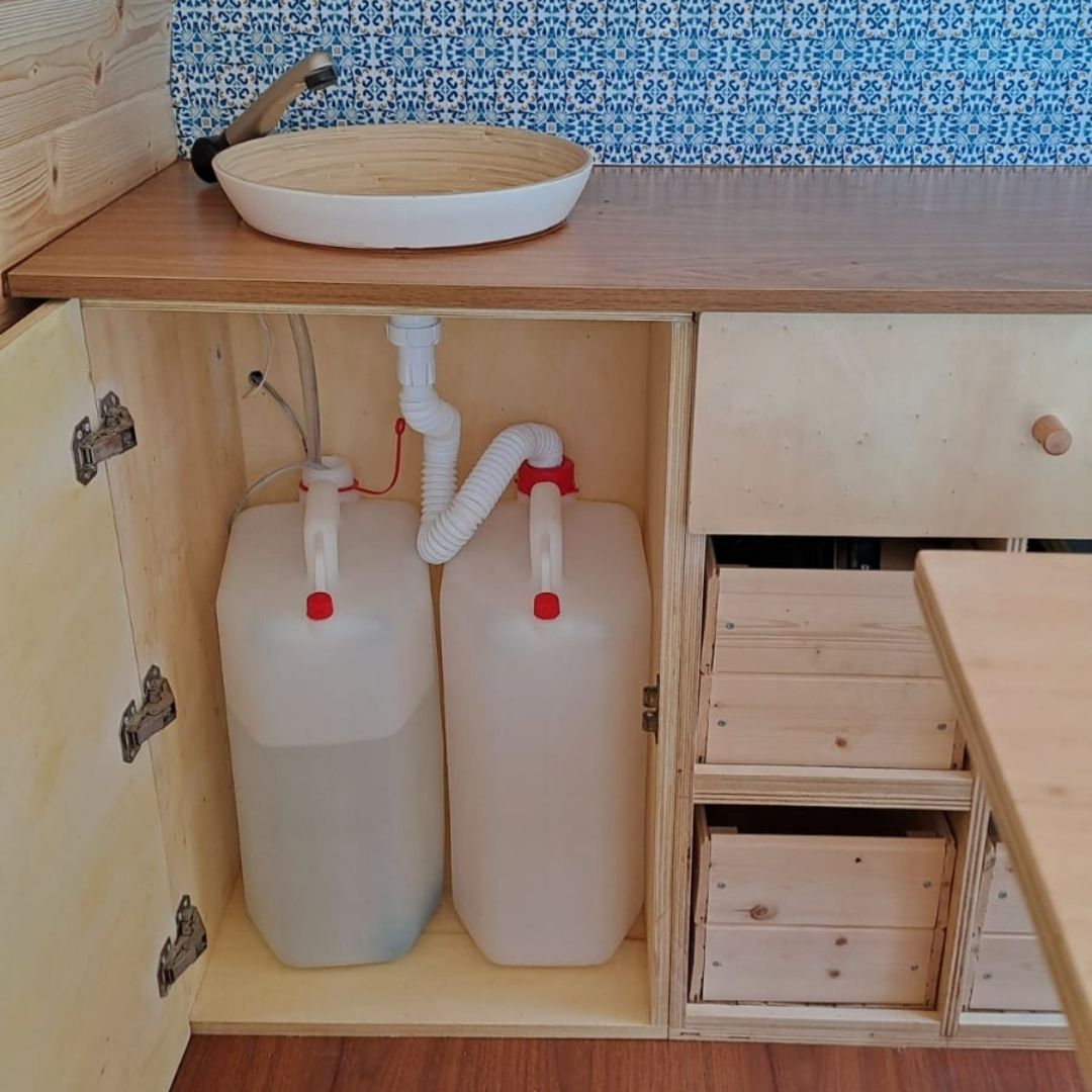 Complete campervan water system kit with 20L tank, 12V pump, and chrome tap laid out for DIY installation in a van conversion